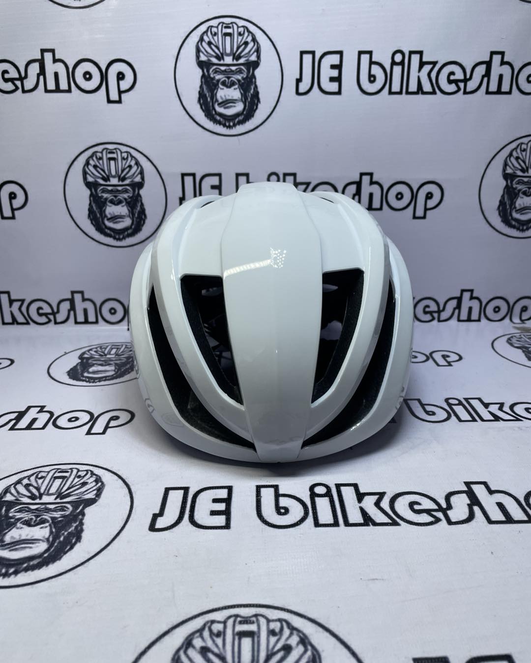 White bicycle helmet on a white background with 'JE Bikeshop' branding.