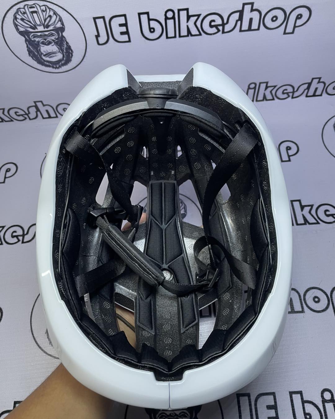 White bicycle helmet with black interior on a white background with 'JE bikeshop' branding.