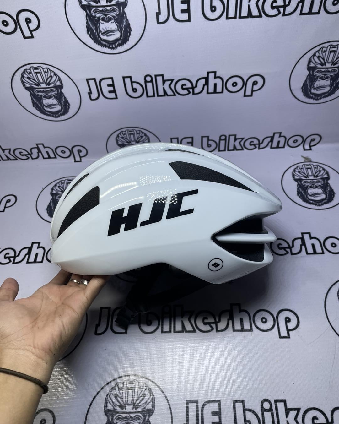 White HJC helmet held by a hand against a branded background